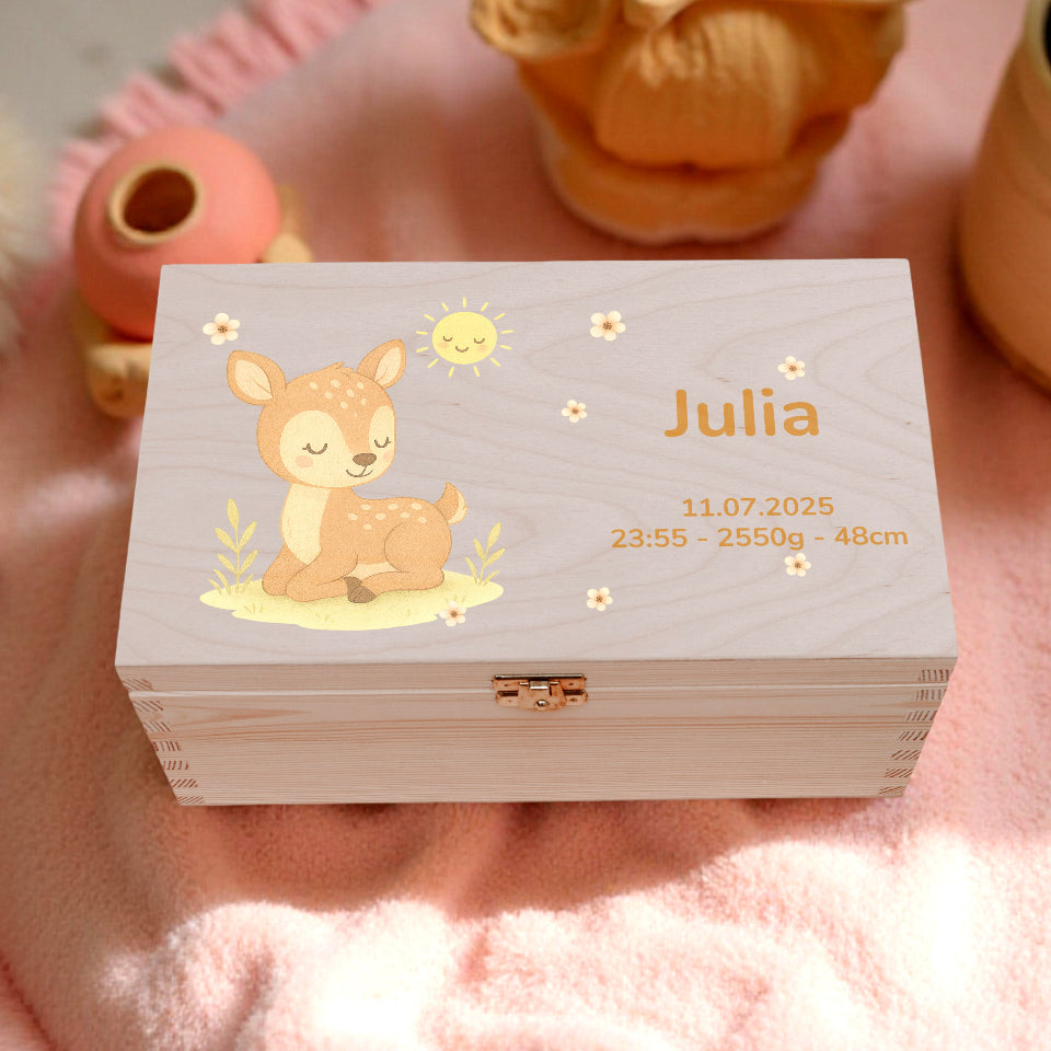 Wooden box with a deer illustration and 'Julia' text on a pink surface with toys and plants.
