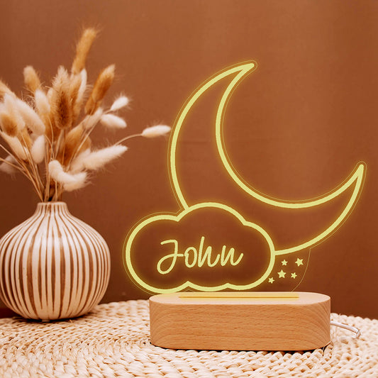 Moon and Cloud Light
Lampka Księżyc z Chmurką z Imieniem
Neon moon-shaped lamp with 'John' on a wooden base next to a vase with dried plants on a textured surface.
