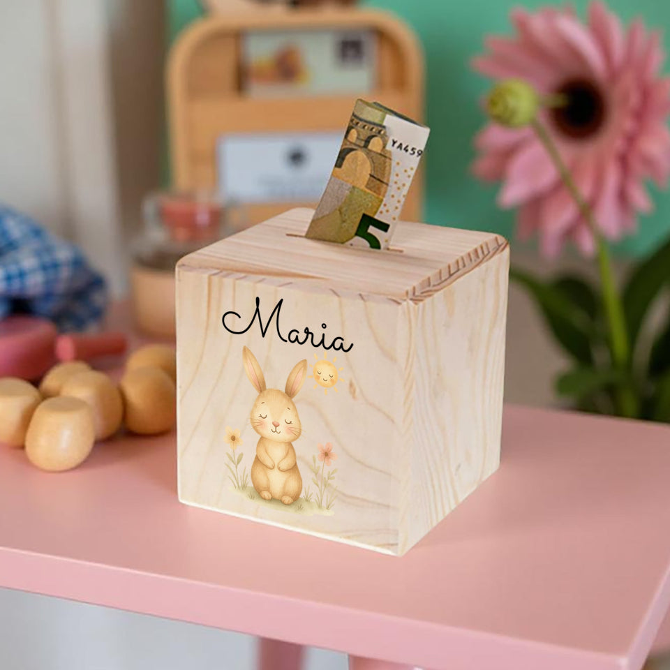 Wooden money box with a rabbit design and the name 'Maria' on a pink surface.