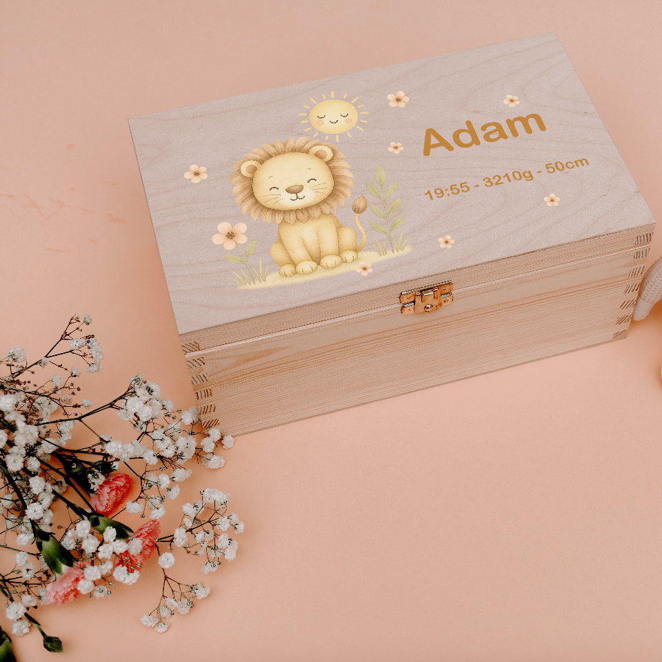 Wooden box with lion illustration and text, accompanied by a stuffed animal and flowers on a pink background