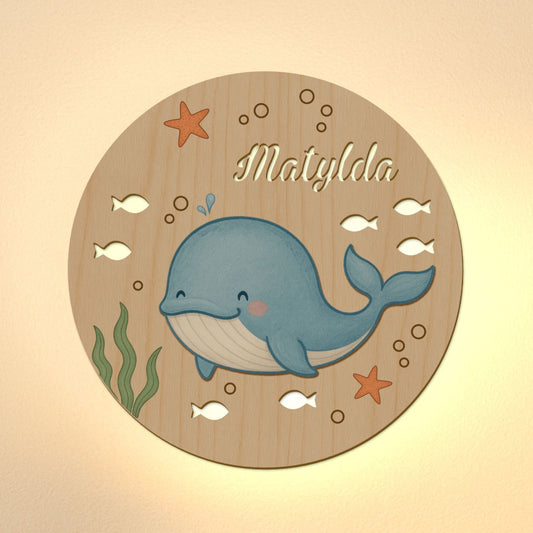Circular wooden plaque with a whale illustration and the name 'Matylda' on a beige background.