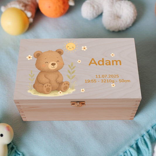Wooden box with teddy bear design and engraved text, surrounded by baby toys on a blue blanket.