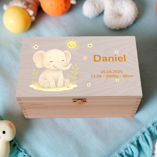 Wooden box with an elephant design and 'Daniel' engraved, surrounded by baby toys on a blue blanket.
