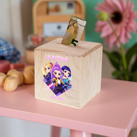 Wooden money box with cartoon characters on a pink surface, surrounded by toys and a flower.