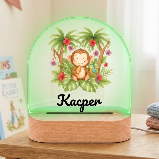 Decorative night light with a monkey design on a wooden surface, surrounded by books and toys.
