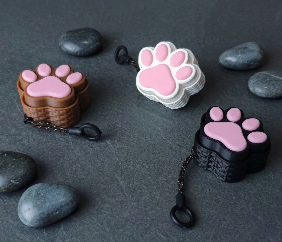 Three paw-shaped keychains on a dark surface with stones.