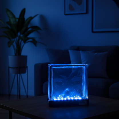 Blue glowing glass block lamp on a table in a dimly lit room with a plant and couch in the background