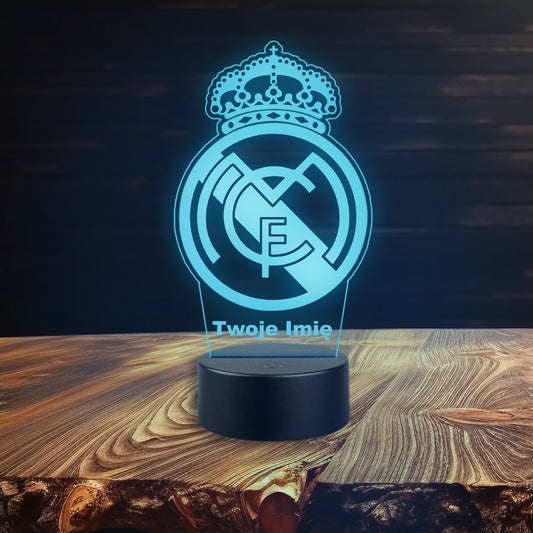 Logo Real Madrytu podświetlone na drewnianym stole, z lampką LED w różnych kolorach, zasilaną kablem lub bateriami.